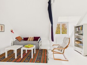 A cozy room with a white sofa, a small table, a rocking chair, and a bookshelf.