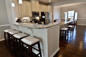 A kitchen with a central island, bar stools, and a dining area with chairs.