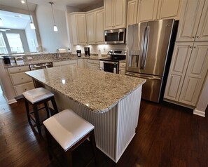 A modern kitchen with granite countertops, stainless steel appliances, and a central island with bar stools.