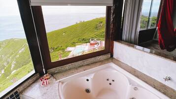 A bathroom with a large bathtub, a view of the ocean, and a window with curtains.