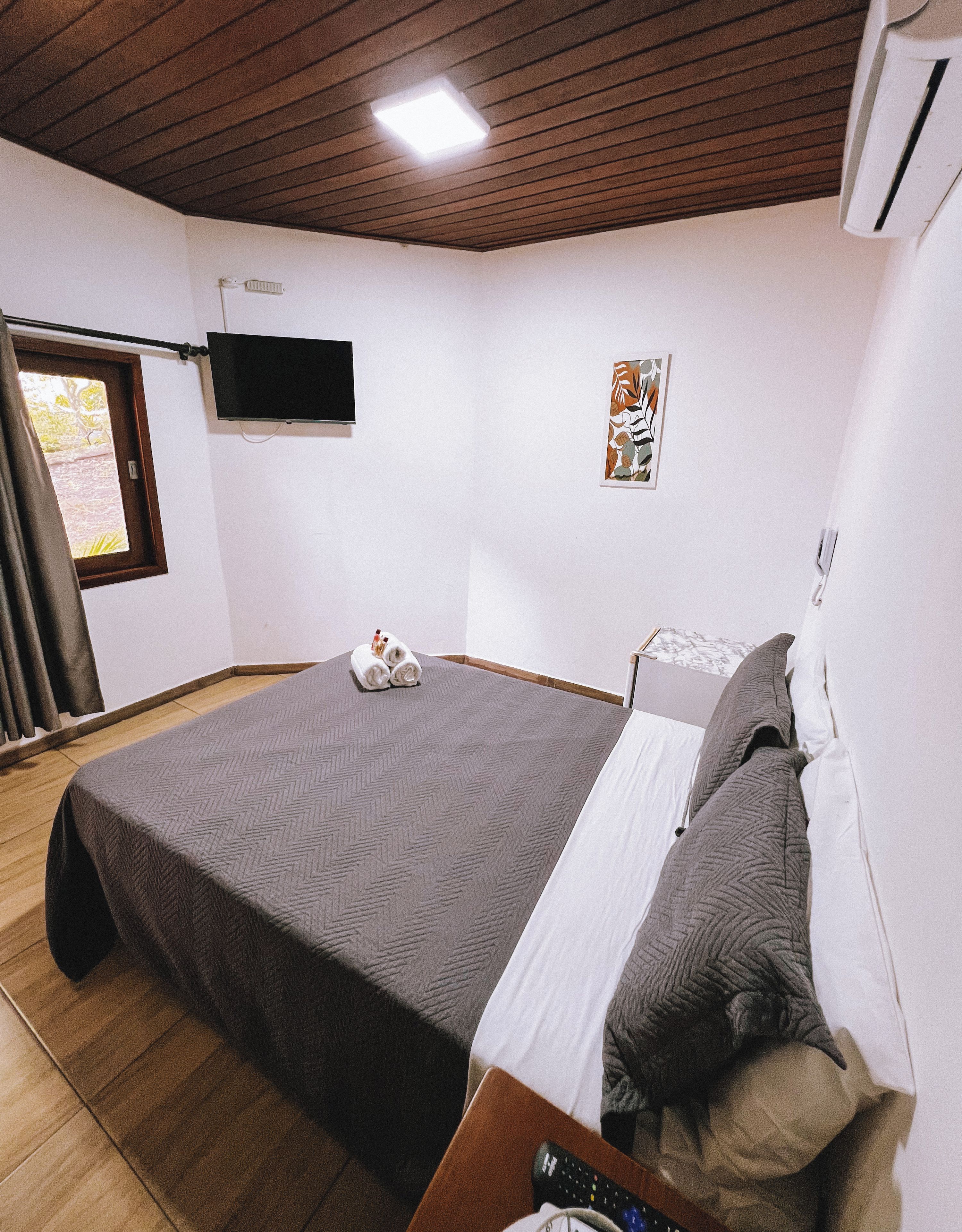 A bedroom with a bed, a flat-screen TV, a poster, and a window.