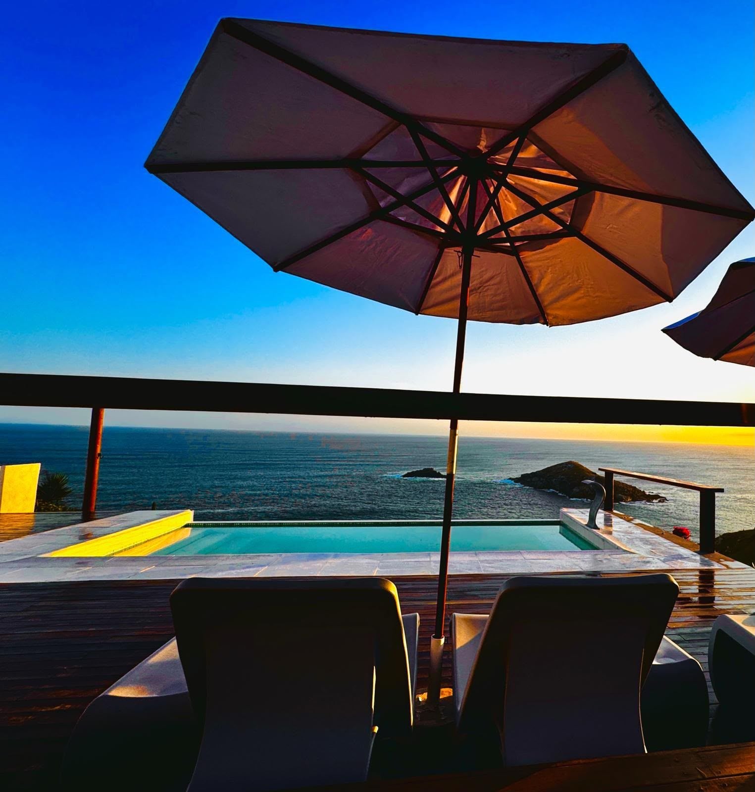 A poolside area with a view of the ocean, a large umbrella, and lounge chairs.