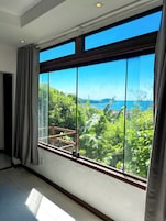 Quarto com uma grande janela com vista para uma paisagem exuberante e um corpo d'água.