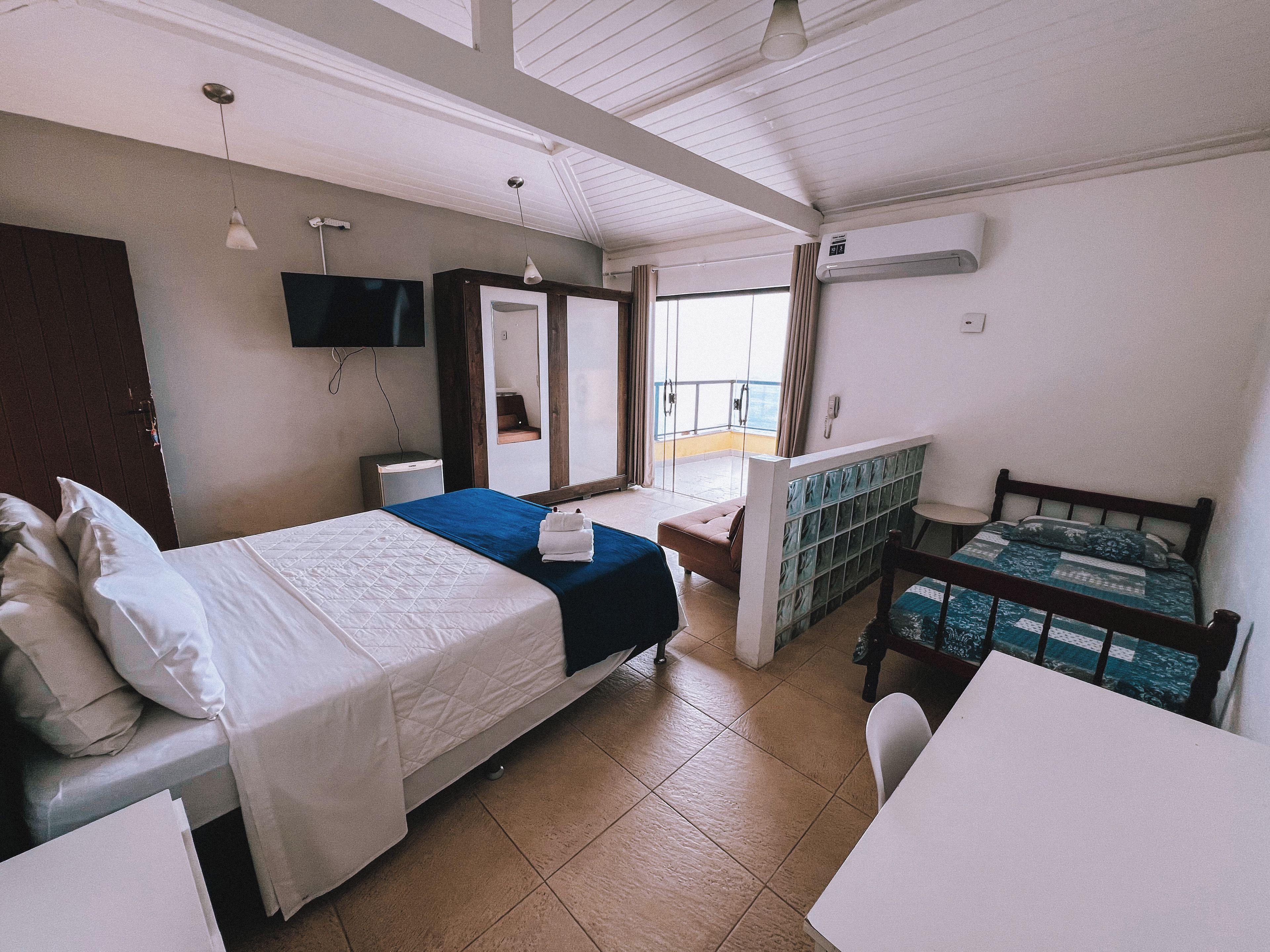 A hotel room with a bed, a desk, a chair, a TV, a mirror, and a window with curtains.