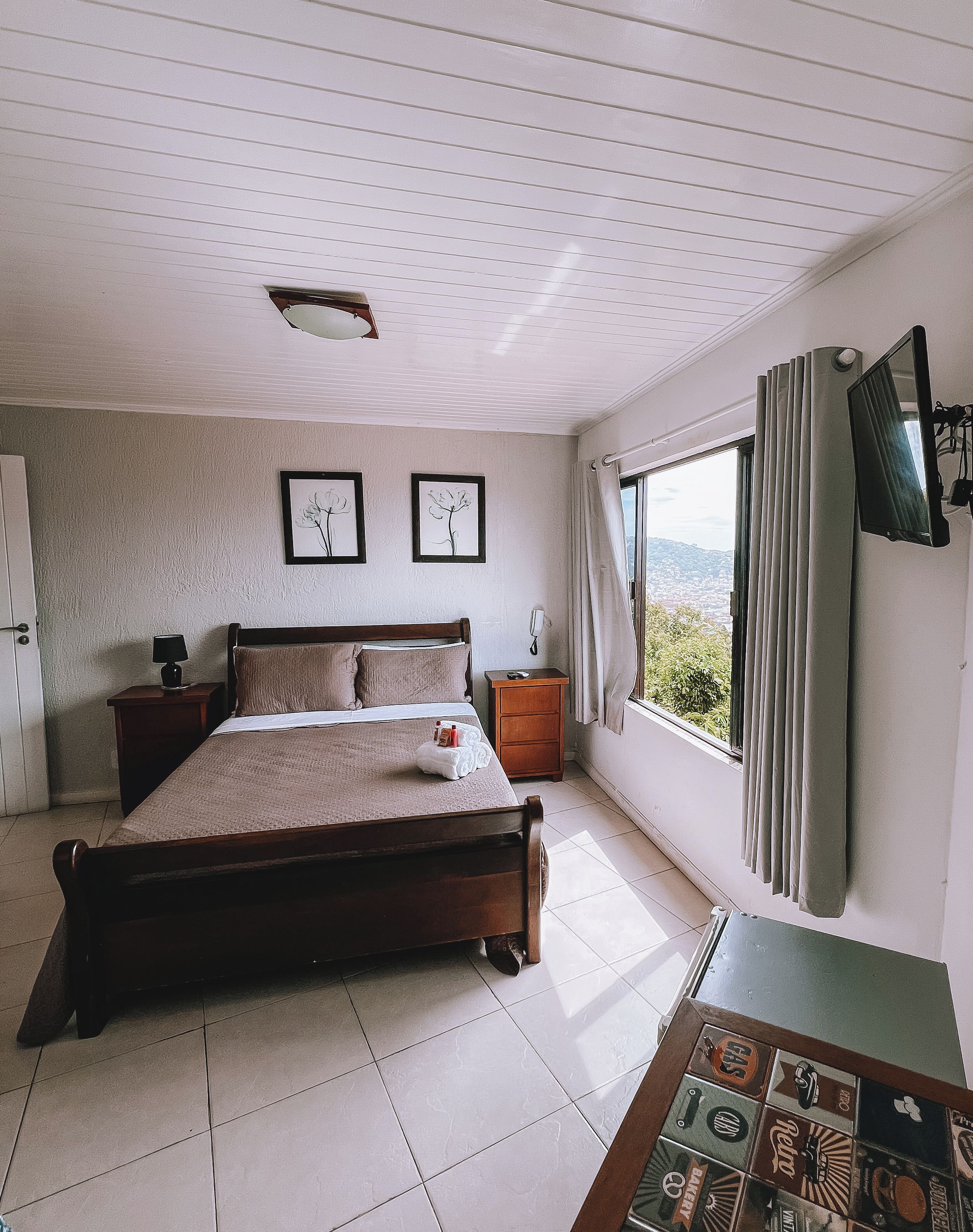 Une chambre à coucher comprenant un lit, une table de chevet, une commode, une fenêtre avec des rideaux et un téléviseur fixé au mur.