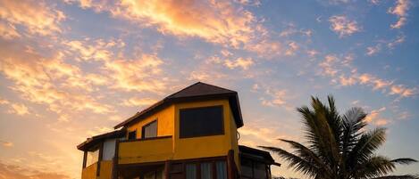 A multi-story building with a balcony, a palm tree, and a sunset sky.