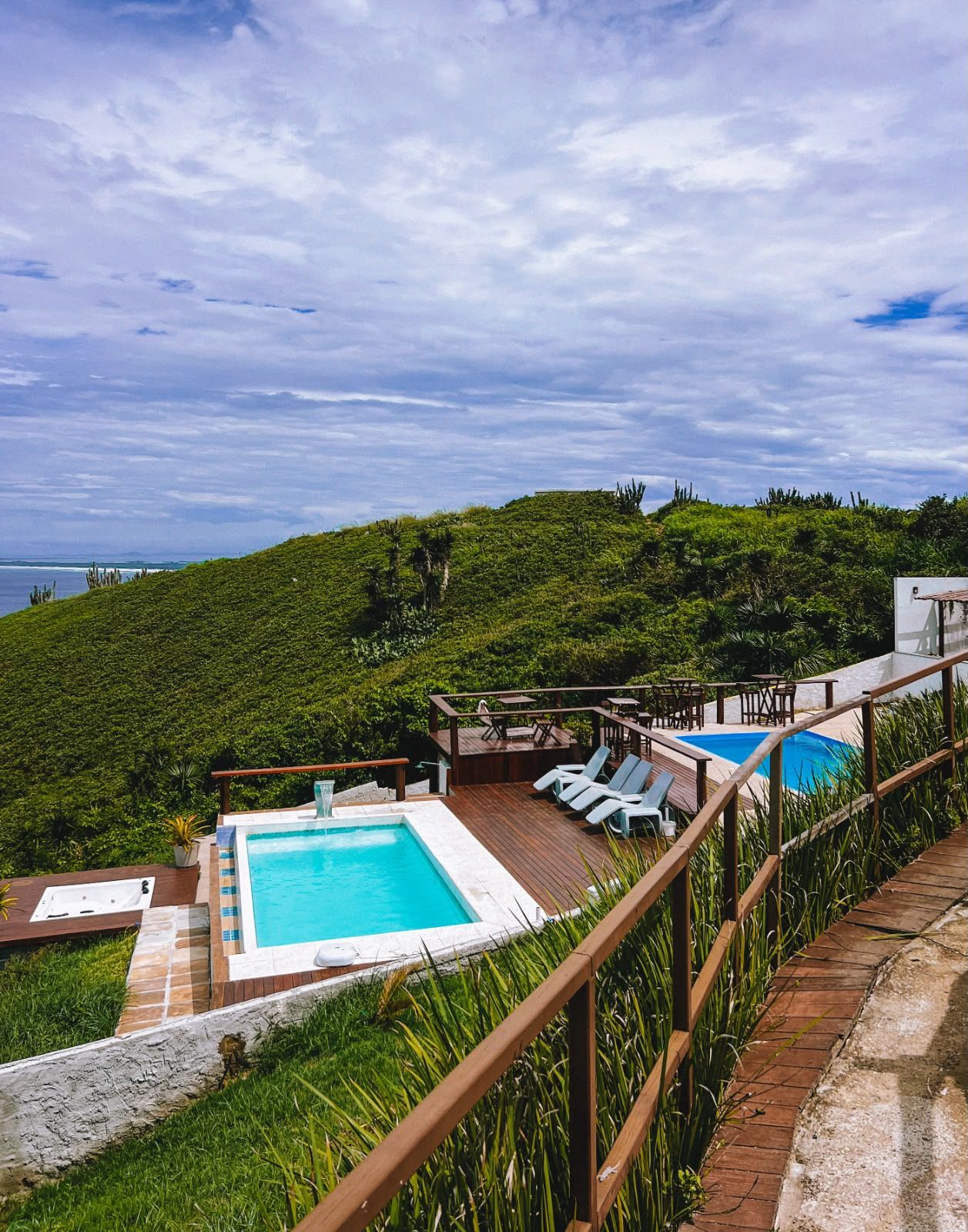 Area piscina con idromassaggio, lettini e terrazza con vista su un verde pendio.