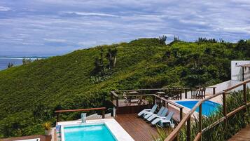 Area piscina con idromassaggio, lettini e terrazza con vista su un verde pendio.
