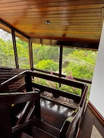 Escadaria de madeira que leva a uma varanda com vista para vegetação exuberante.
