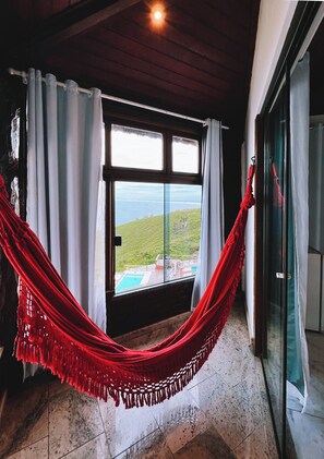 Una habitación con un ventanal grande, una hamaca roja y vistas a un paisaje verde.