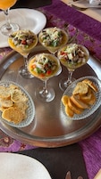 A tray with three glasses of seafood cocktail, two plates of bread, and a glass of orange juice.