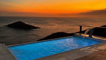 Una piscina con un pontile in legno e vista sull'oceano al tramonto.