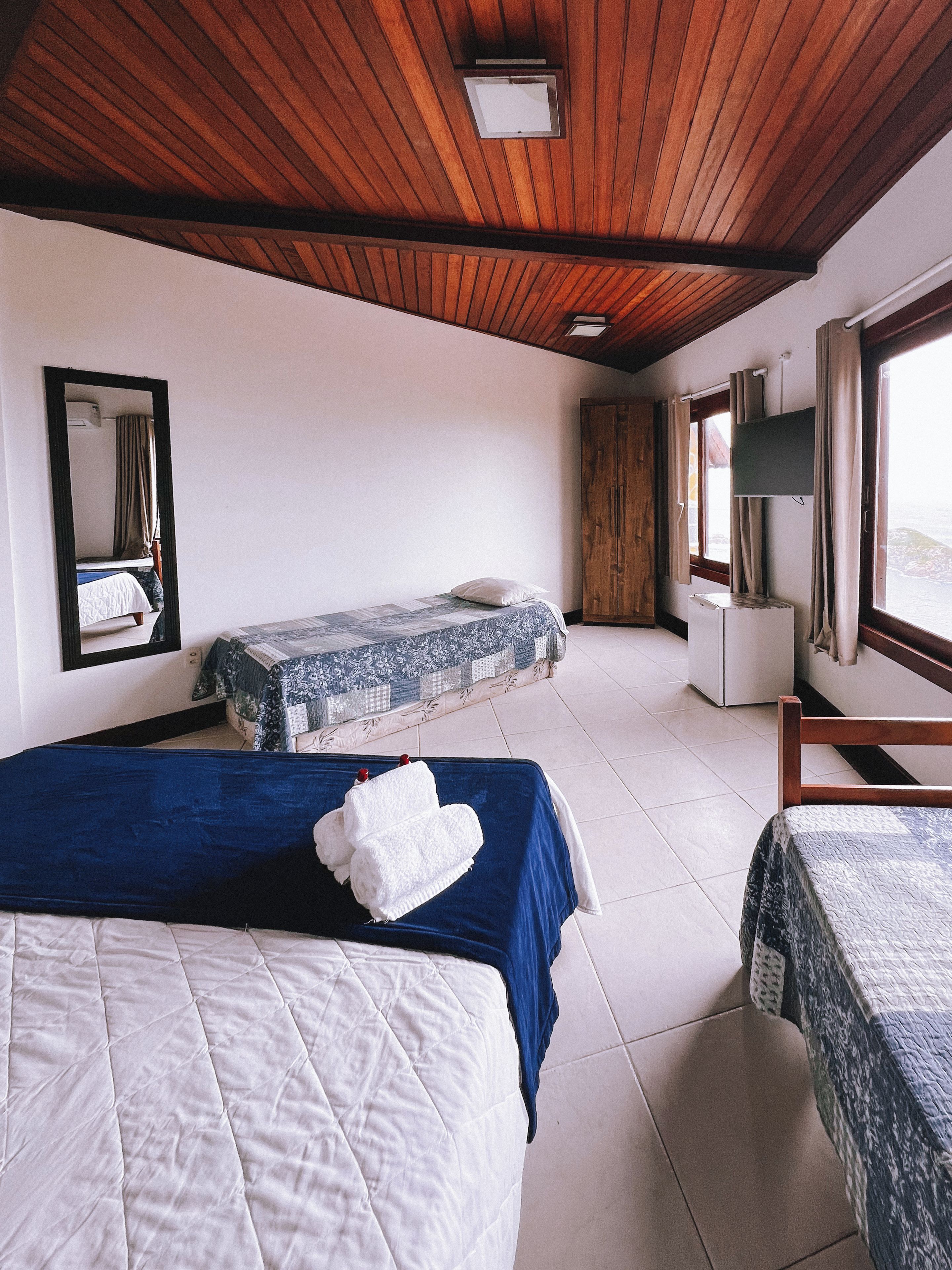 A hotel room with two beds, a large mirror, a television, and a view of the sea.