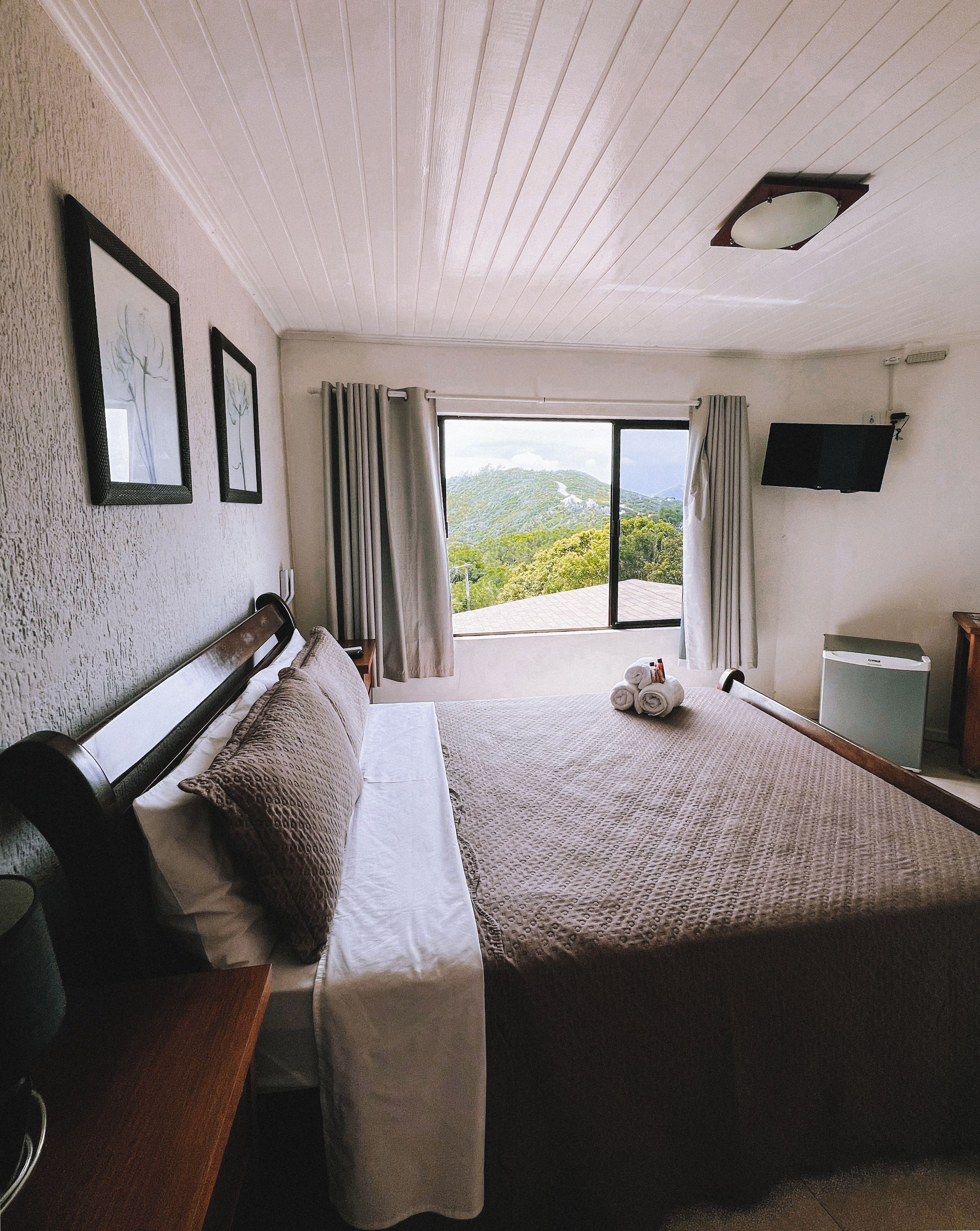 A hotel room with a large bed, a desk, a chair, a flat-screen TV, and a view of the outdoors.