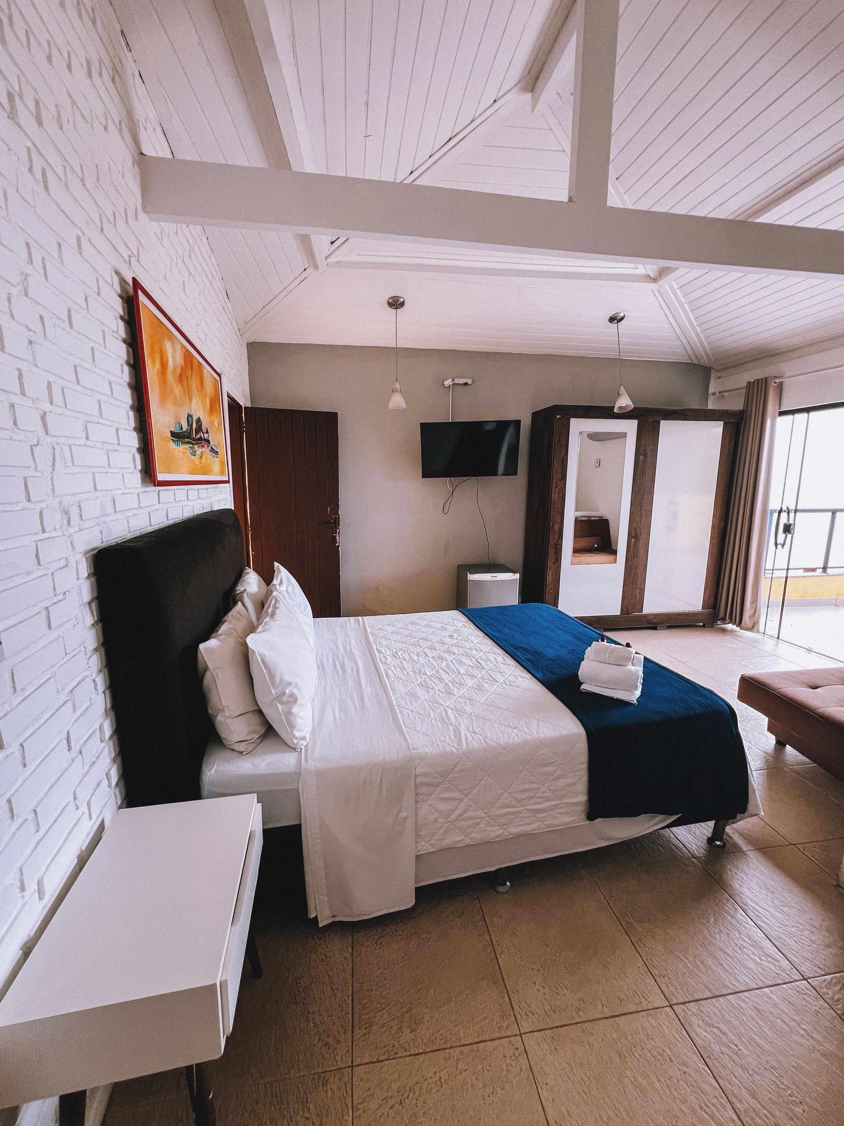 Habitación de hotel con cama, escritorio, televisor montado en la pared y ventana con cortinas.