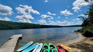 A wooden dock extending into a calm lake with kayaks lined up on the shore.