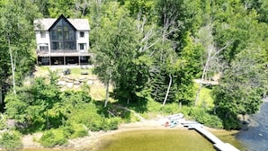 A two-story house with a balcony, surrounded by dense forest and a lake.