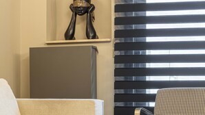 A modern living room with a sofa, a coffee table with books, a decorative sculpture, and a window with blinds. - ICONIC SALONICA SUITE seafront (Thessaloniki)