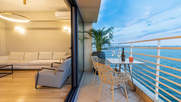 A balcony with a sofa, chairs, and a table with a plant and a bottle. - ICONIC SALONICA SUITE seafront (Thessaloniki)