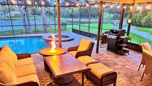 Een terras buiten met rieten meubilair, een vuurkuil en een barbecuehoek.