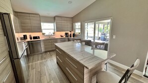 Een moderne keuken met houten kastjes, een groot eiland en een zithoek buiten.