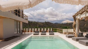 A poolside area with a clear view of the landscape, including a building with a balcony and outdoor seating. - Xeno Hotel Boutique (San Pedro Pochutla)