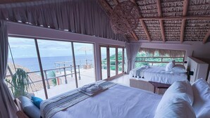 A bedroom with a large bed, a view of the sea, and a thatched roof. - Xeno Hotel Boutique (San Pedro Pochutla)