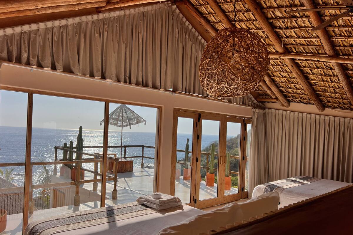 A room with a large window, a bed, and a view of the sea.