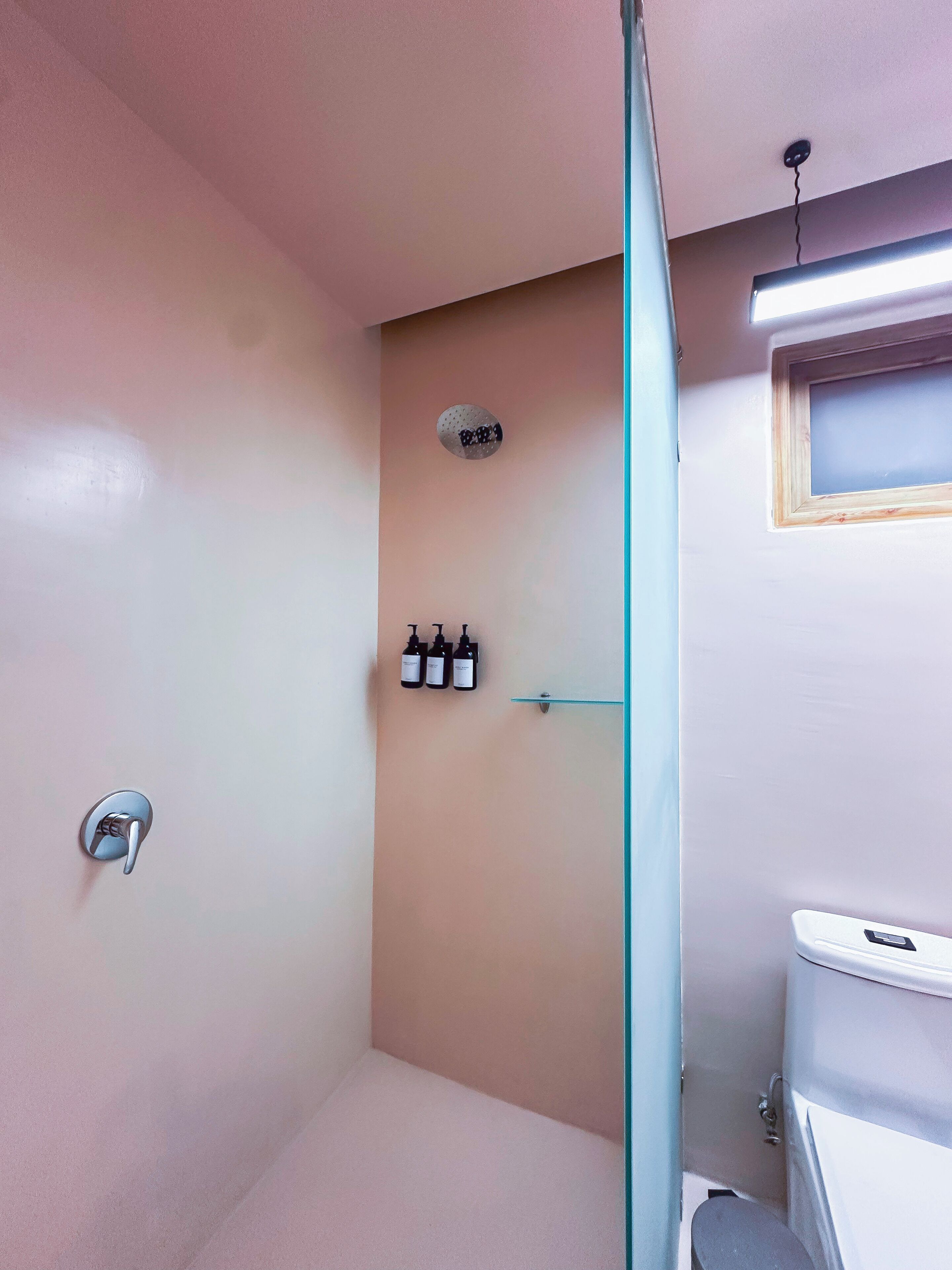 Een badkamer met een douche, toilet en wastafel. Boven het toilet staan drie flessen.