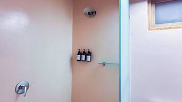 Een badkamer met een douche, toilet en wastafel. Boven het toilet staan drie flessen.