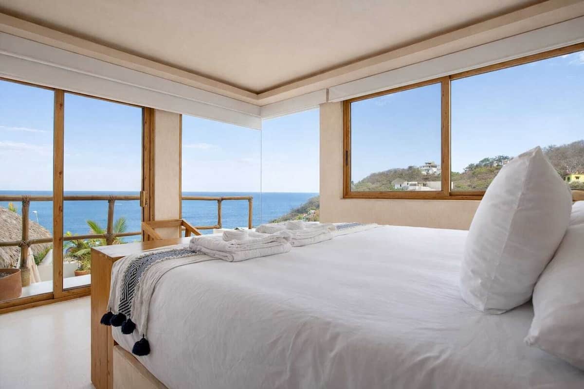 A bedroom with a large bed, a view of the sea, and a balcony with wooden railings.