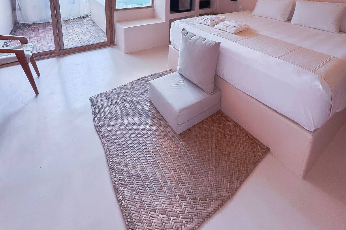 A modern bedroom with a large bed, a ceiling fan, a TV, and a sliding glass door leading to an outdoor area.