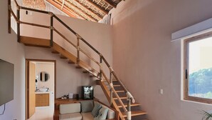 A modern interior with a wooden staircase, a sofa, a television, and a window with a view. - Xeno Hotel Boutique (San Pedro Pochutla)