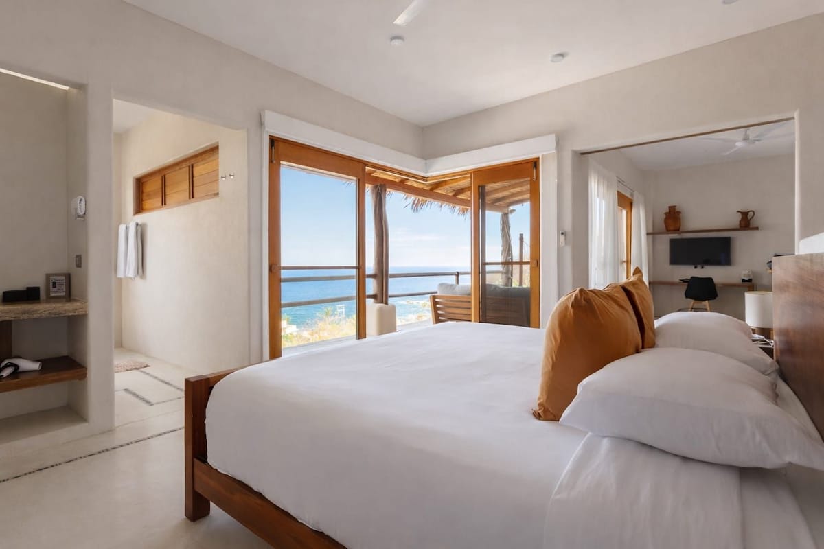 Un dormitorio con una cama grande, cabecera de madera, televisor y vista al mar.