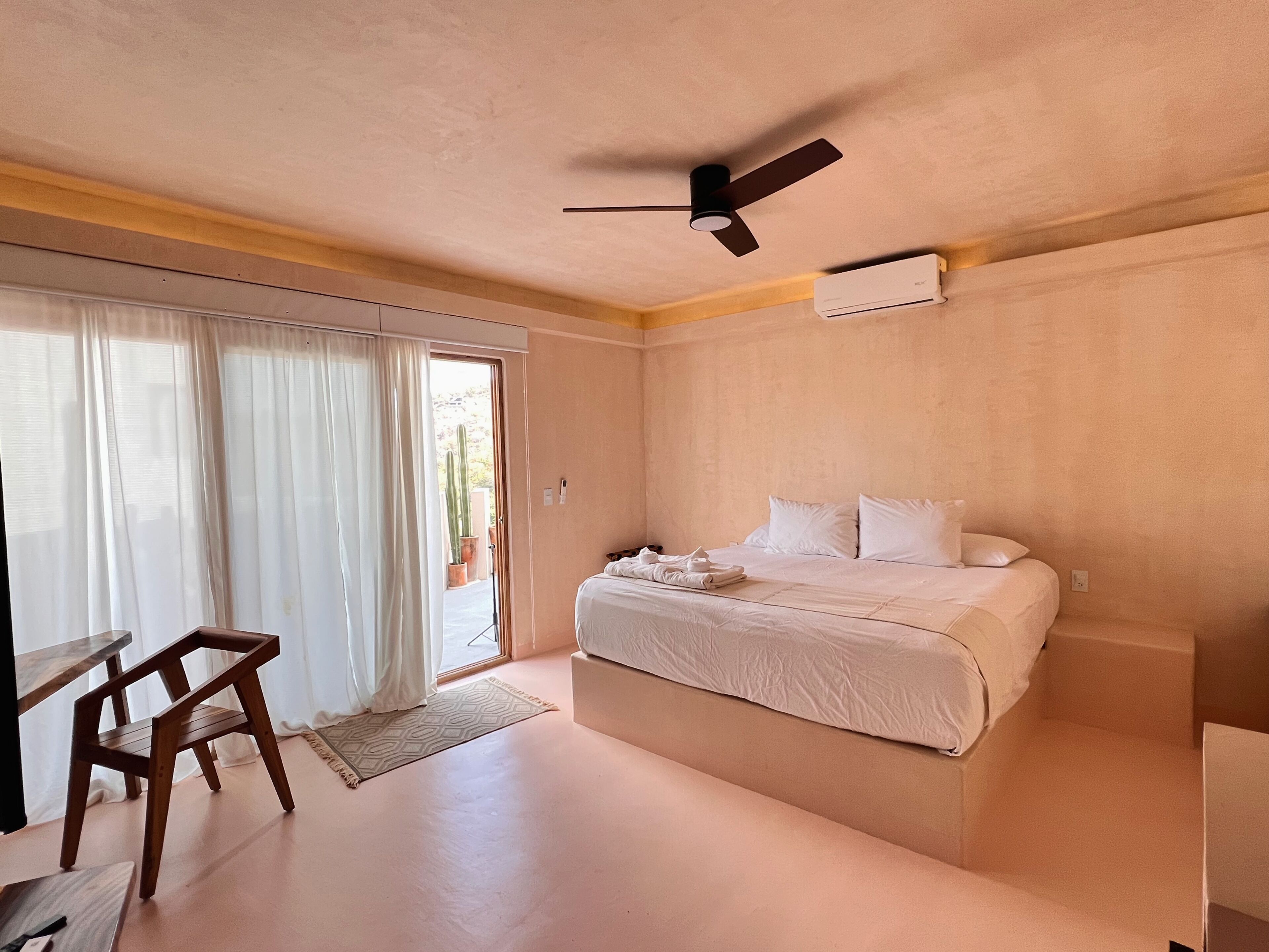 Quarto com cama, ventoinha no teto, janela com cortinas e vista para o exterior.