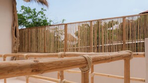 A wooden deck with a thatched roof, bamboo fence, and a view of trees and buildings in the background. - Xeno Hotel Boutique (San Pedro Pochutla)