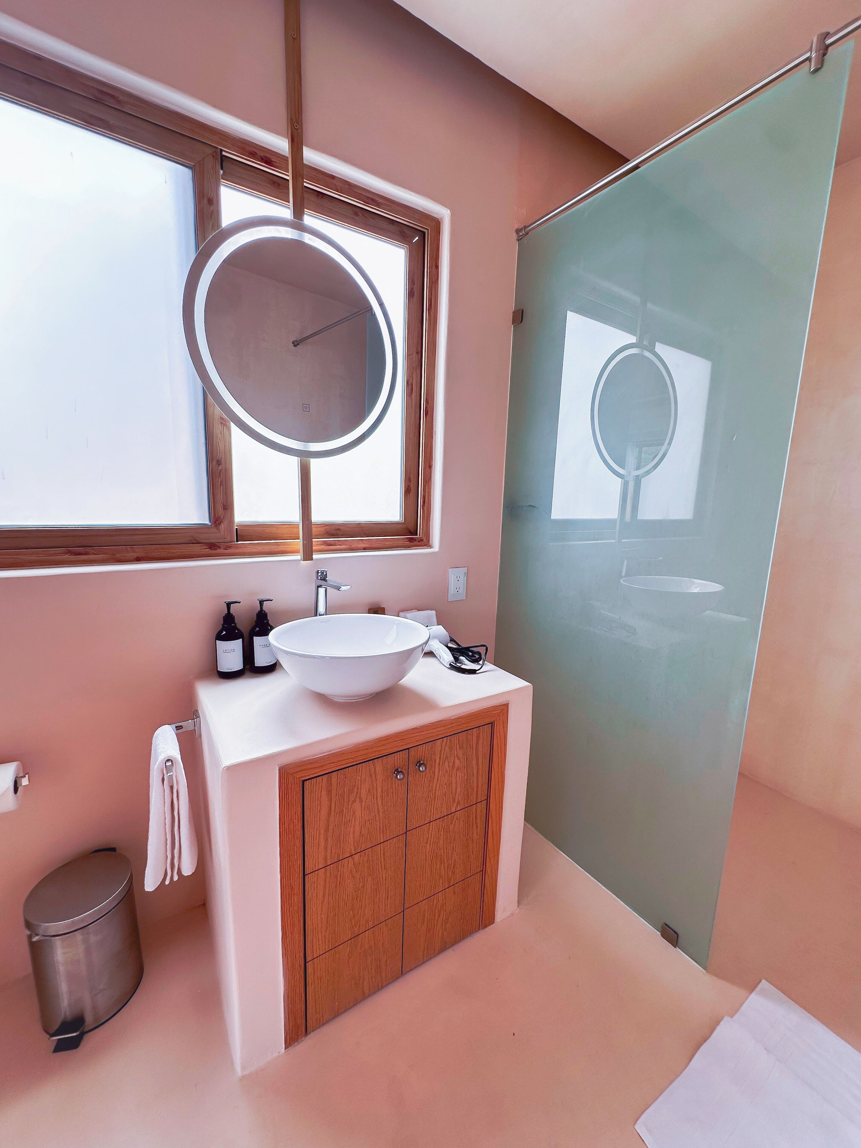 Un baño moderno con un espejo redondo grande, un lavamanos blanco y armarios de madera.