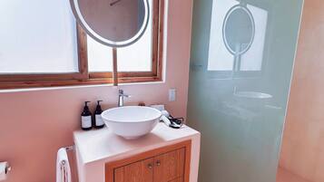 Un baño moderno con un espejo redondo grande, un lavamanos blanco y armarios de madera.