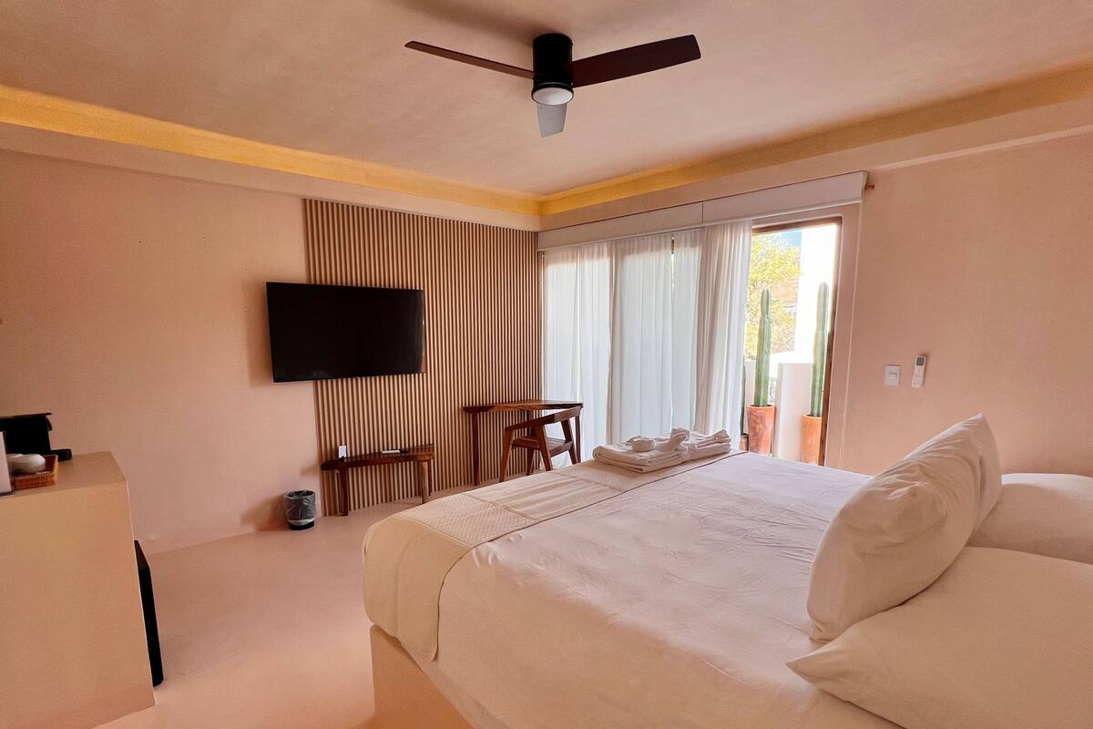 A hotel room with a bed, a desk, a chair, a television, and a ceiling fan.