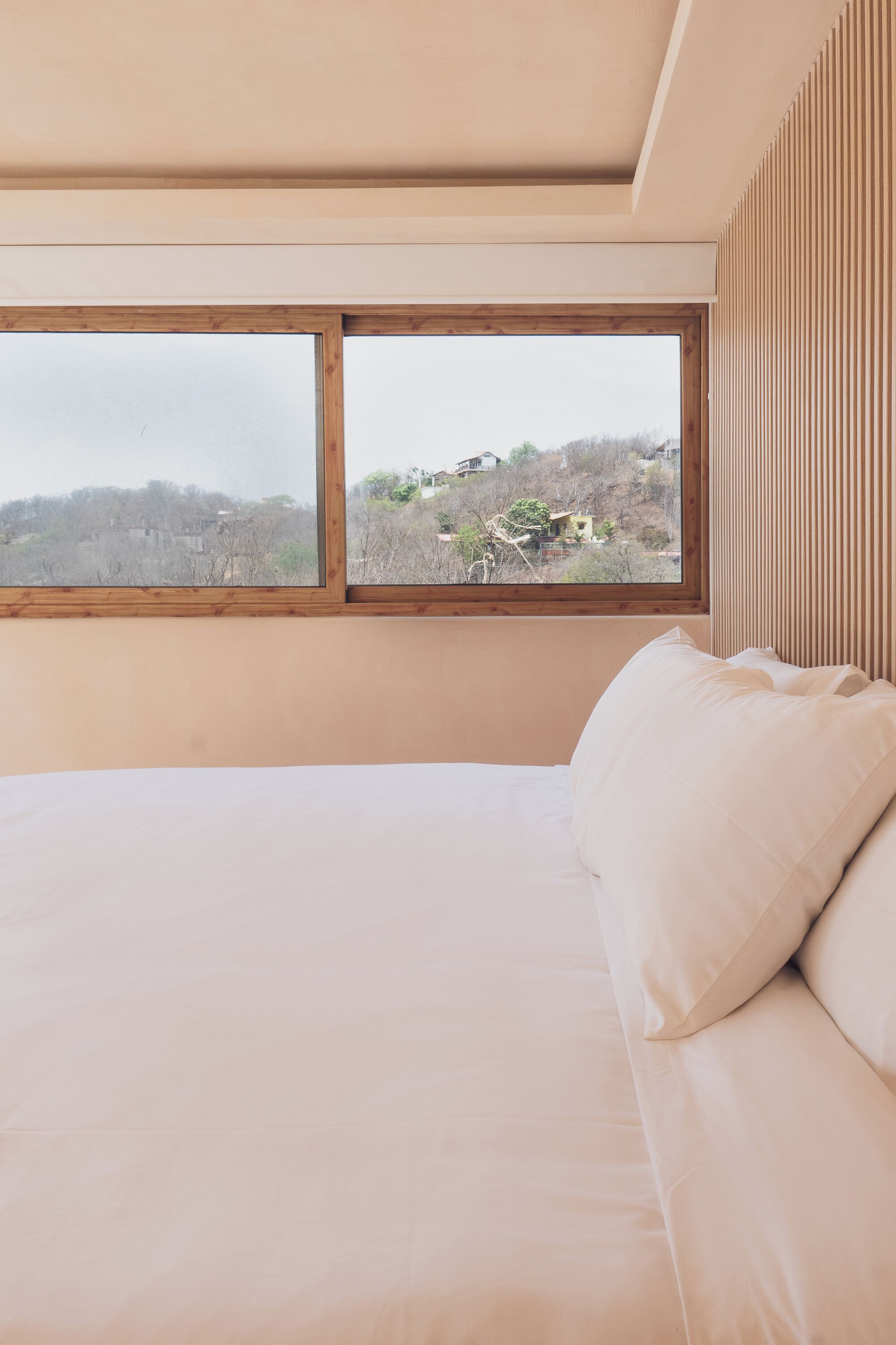Un dormitorio con una cama grande, cabecero de madera y vistas a un paisaje montañoso a través de dos ventanas.