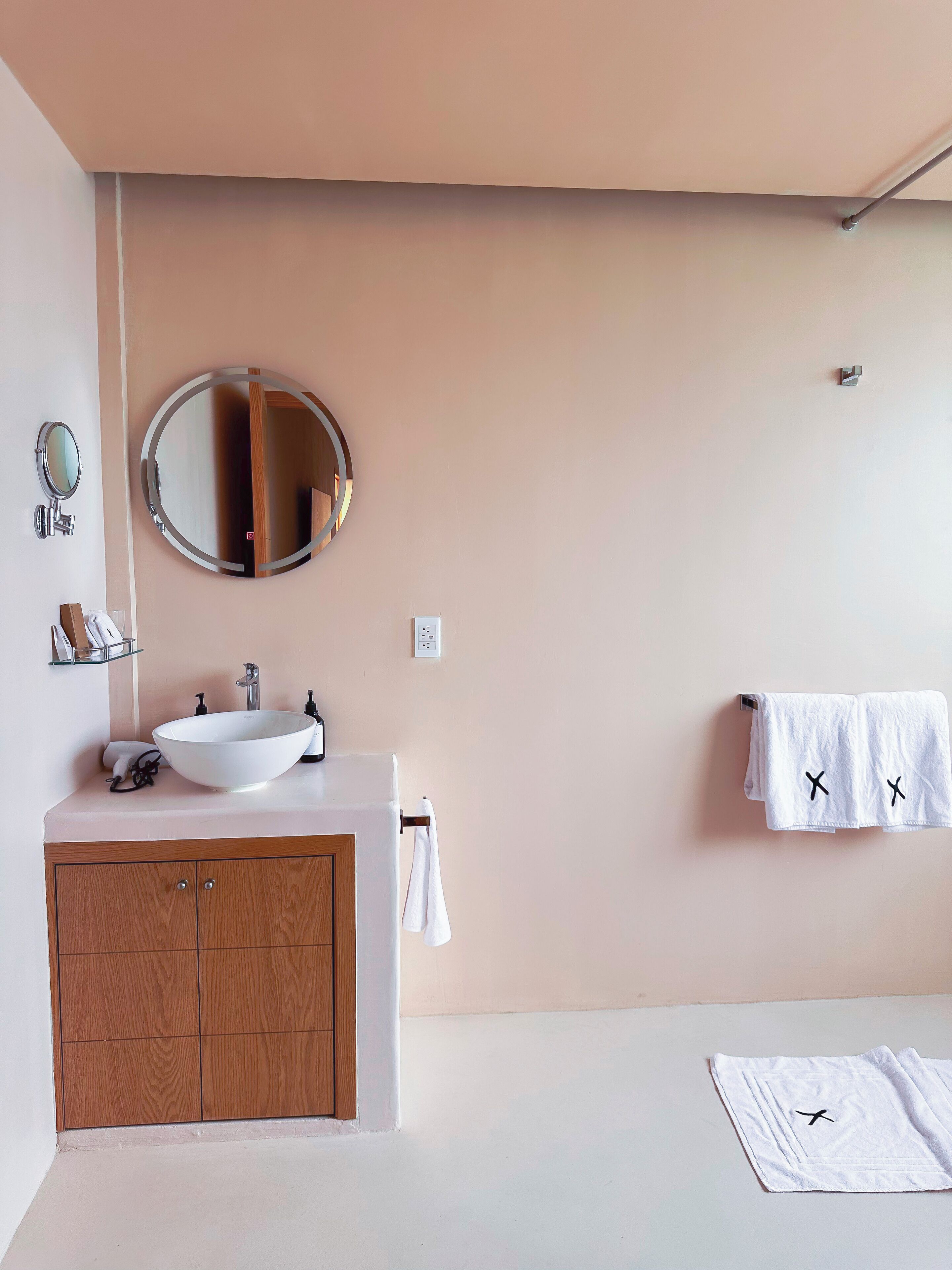 A modern bathroom with a wooden vanity, a round mirror, and a towel rack with two towels.