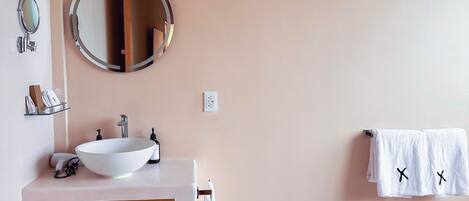 A modern bathroom with a wooden vanity, a round mirror, and a towel rack with two towels.
