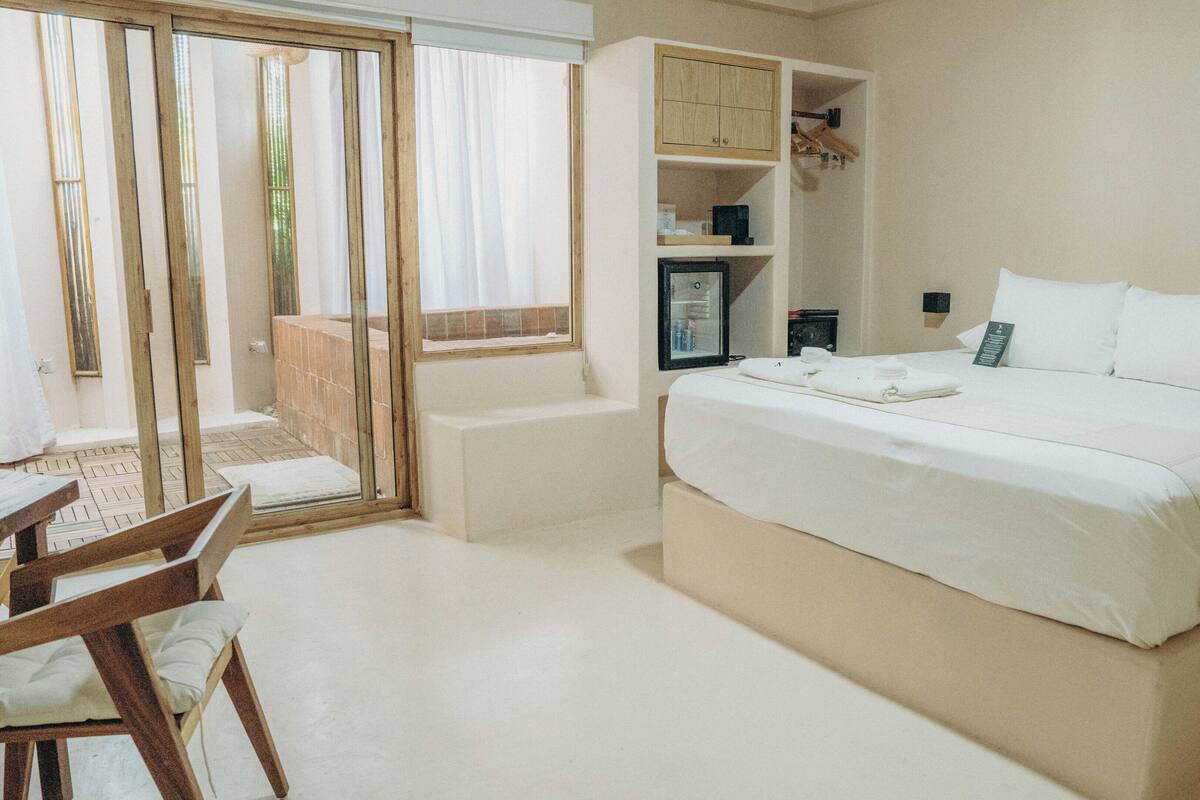 A bedroom with a bed, a wooden chair, a small table, a cabinet, and a sliding glass door leading to an outdoor area.