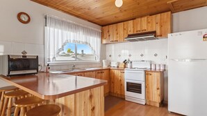Eine Küche mit Holzschränken, einem Backofen, einem Kühlschrank und einem Fenster mit Vorhängen.