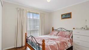 Ein Schlafzimmer mit Bett, Kommode, einem Fenster mit Vorhängen und einem Bild an der Wand.