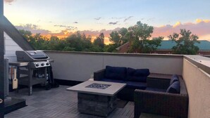 A rooftop patio with a grill, outdoor seating, and a view of trees and a sunset. - Highlands Home with Rocky Mountain Views! (Denver)