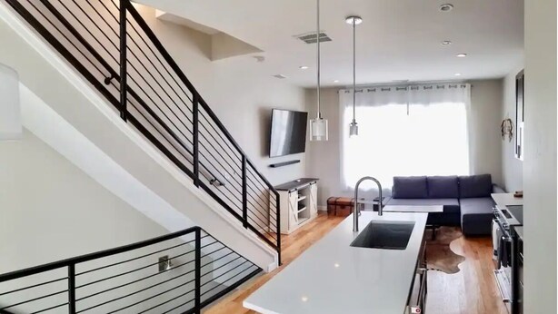 A modern kitchen with a central island, a dining area with a sofa, and a staircase with black railings. - Highlands Home with Rocky Mountain Views! (Denver)