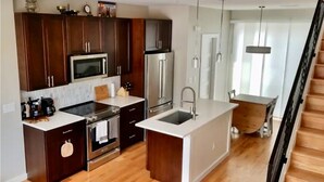 A modern kitchen with dark wooden cabinets, stainless steel appliances, and a central island with a sink. - Highlands Home with Rocky Mountain Views! (Denver)