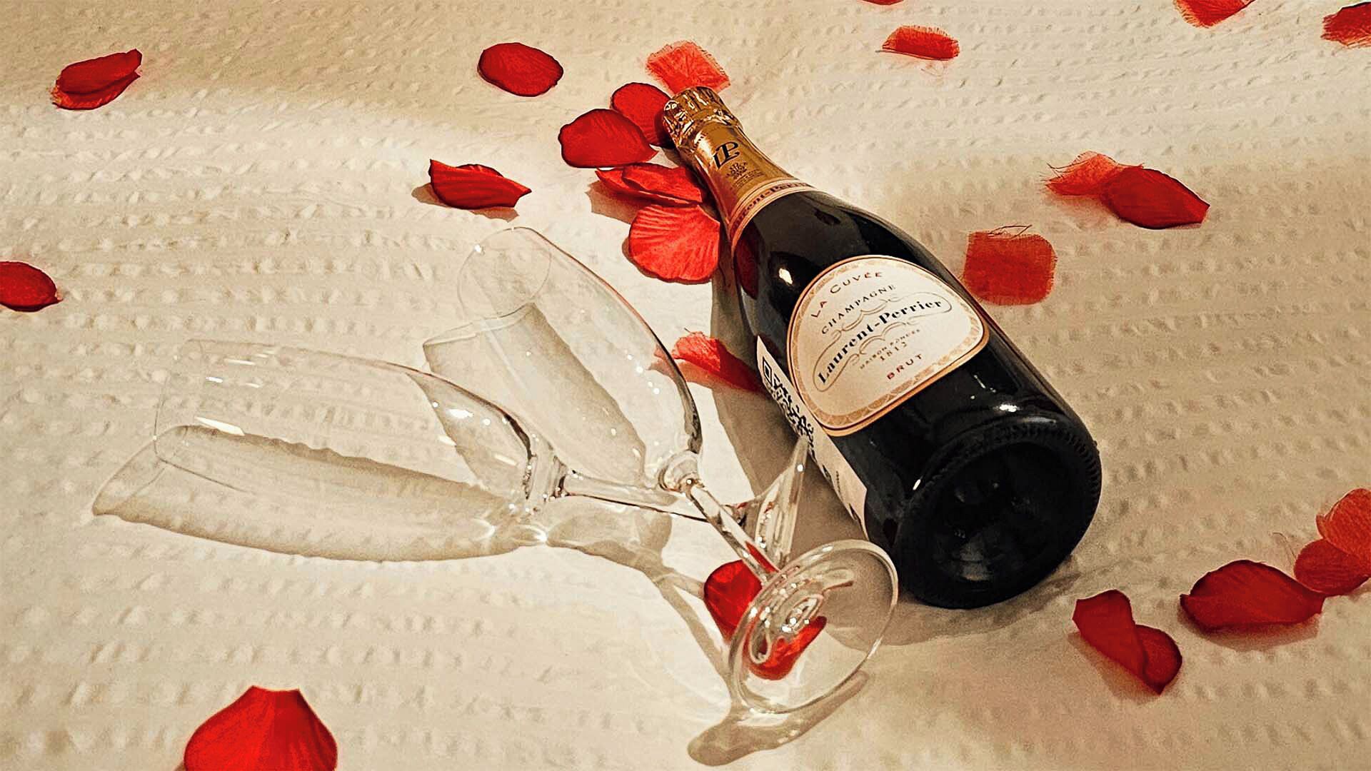 Une bouteille de champagne et un verre posés sur une surface texturée, parsemée de pétales de rose.