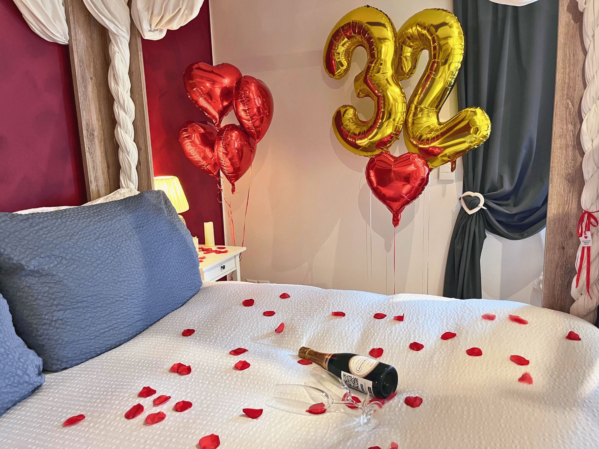 Un dormitorio con cama, una botella de champán y globos con forma de corazón.